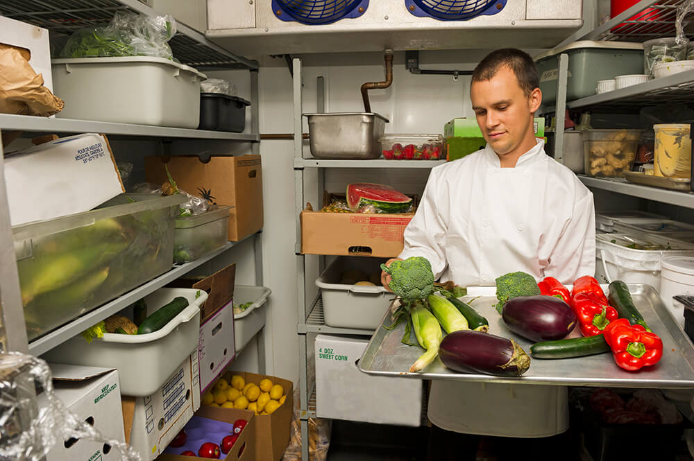 chef standing in a wlak-in -cooler with fresh vegetables