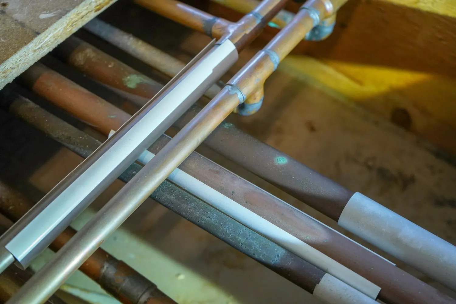 A close-up view shows multiple copper pipes, some with white insulation, running through wooden framing, indicating a repiping installation or repair.