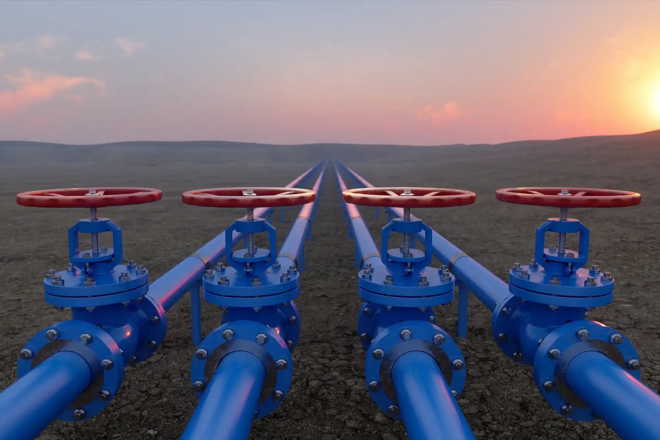 Four blue industrial pipelines with red valve wheels stretching across barren landscape at sunrise or sunset, symbolizing energy infrastructure and utility systems