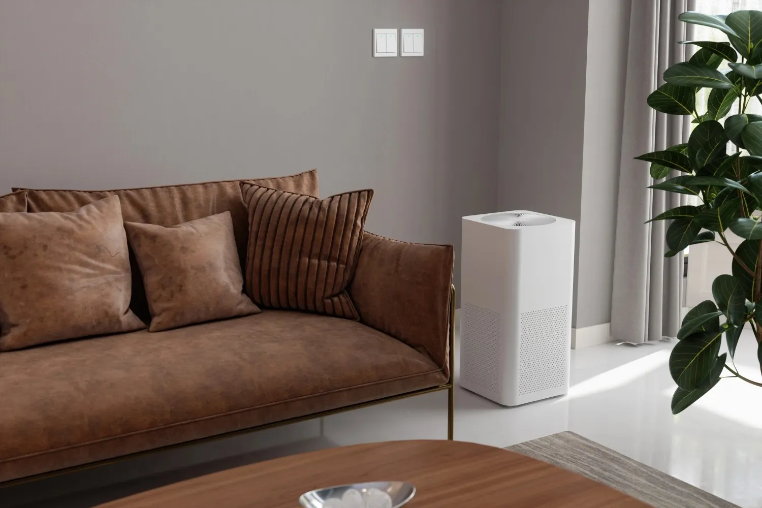 A modern white rectangular whole house dehumidifier stands on a shiny white floor in a living room positioned between a brown sofa with pillows and a large green plant